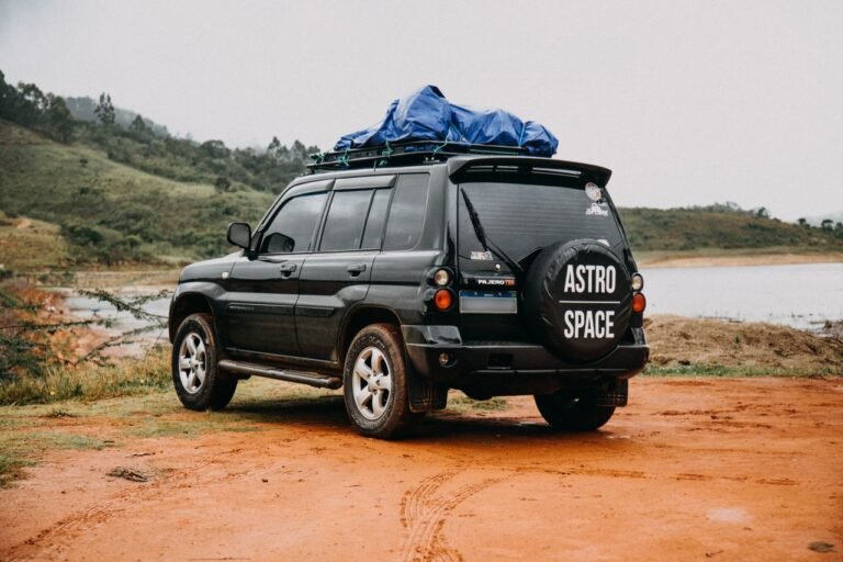 A Mitsubishi Pajero SUV parked near a lakeside with a view of green hills, perfect for adventure travel enthusiasts.