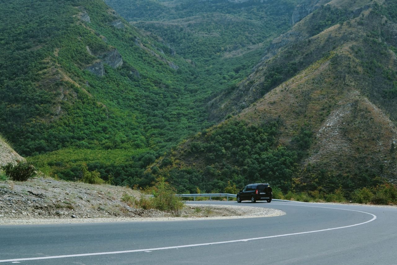A black car navigating a winding road through lush green mountains, perfect for travel themes.