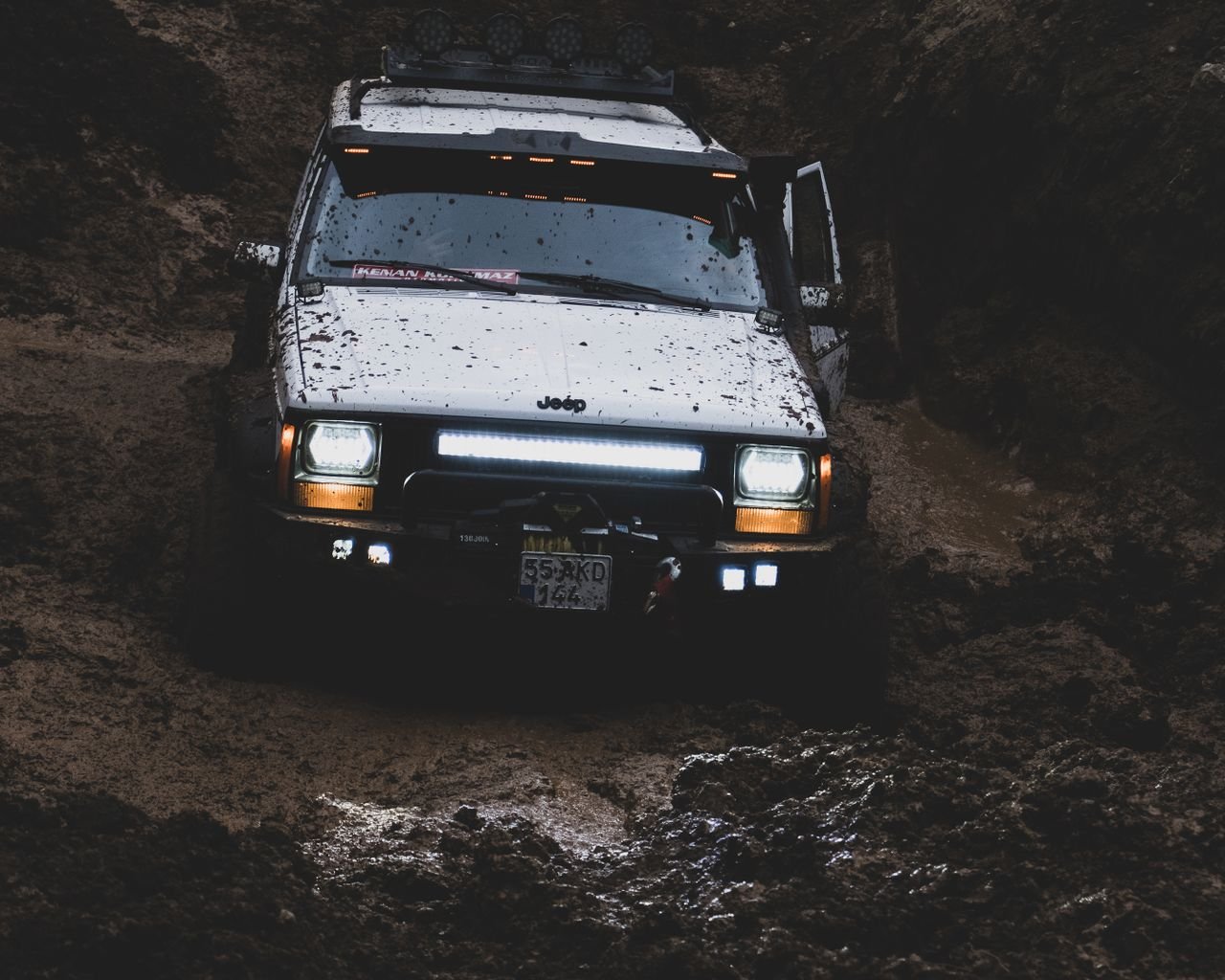 A rugged Jeep Cherokee navigating through a muddy offroad terrain, showcasing its capability.