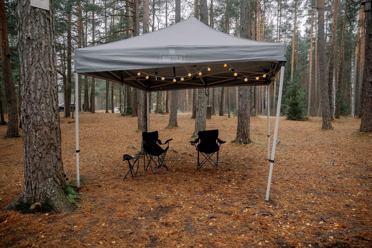 A serene forest campsite with a canopy tent and chairs, perfect for outdoor relaxation.