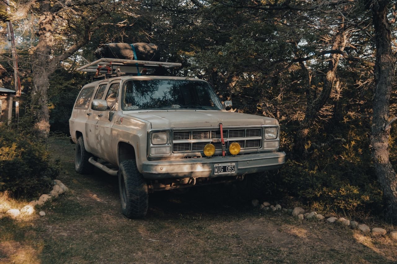 An old SUV parked in a forest, ready for adventure travel with rooftop luggage.