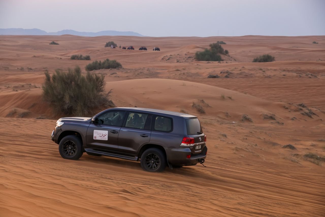 SUV driving through expansive desert dunes during sunset, showcasing adventure and natural beauty.