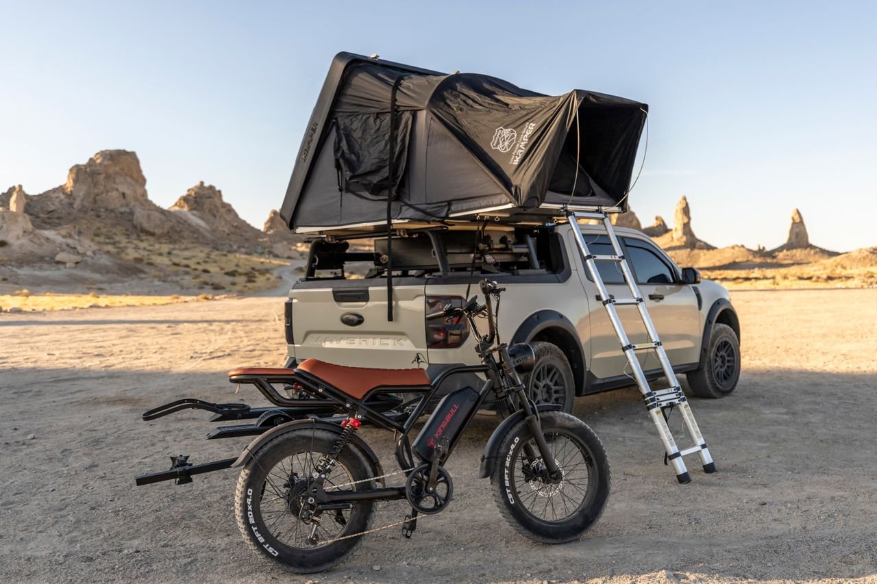 Truck with rooftop tent and mountain bike in desert landscape, perfect backdrop for an outdoor adventure.