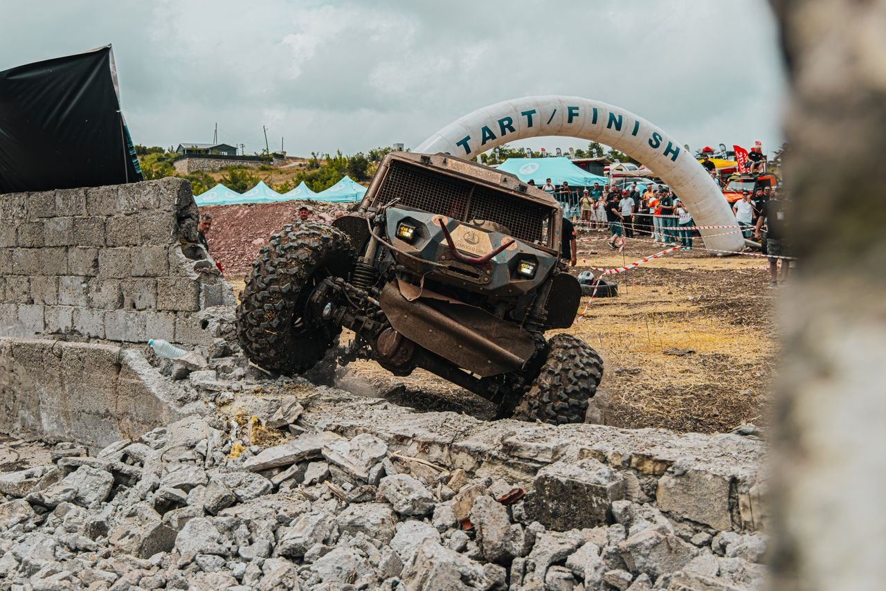 An offroad vehicle tackles a challenging course at an outdoor racing event with spectators watching eagerly.