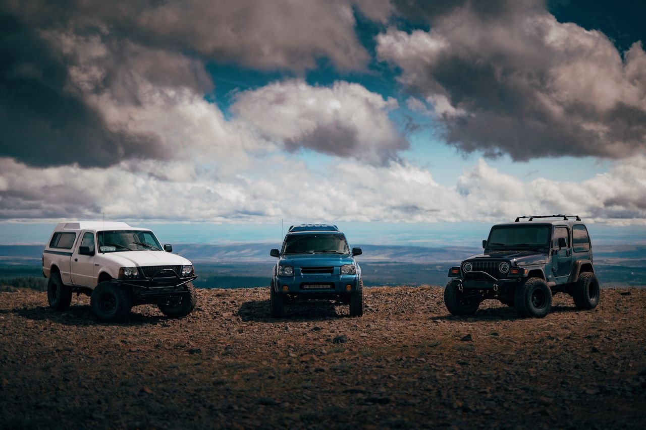 Various contemporary style all terrain vehicles parked on dry shabby terrain behind mounts under dramatic cloudy sky in overcast weather in daylight