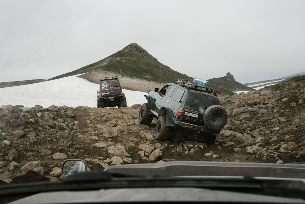 Two jeeps maneuvering a rocky, remote mountain path under an overcast sky.