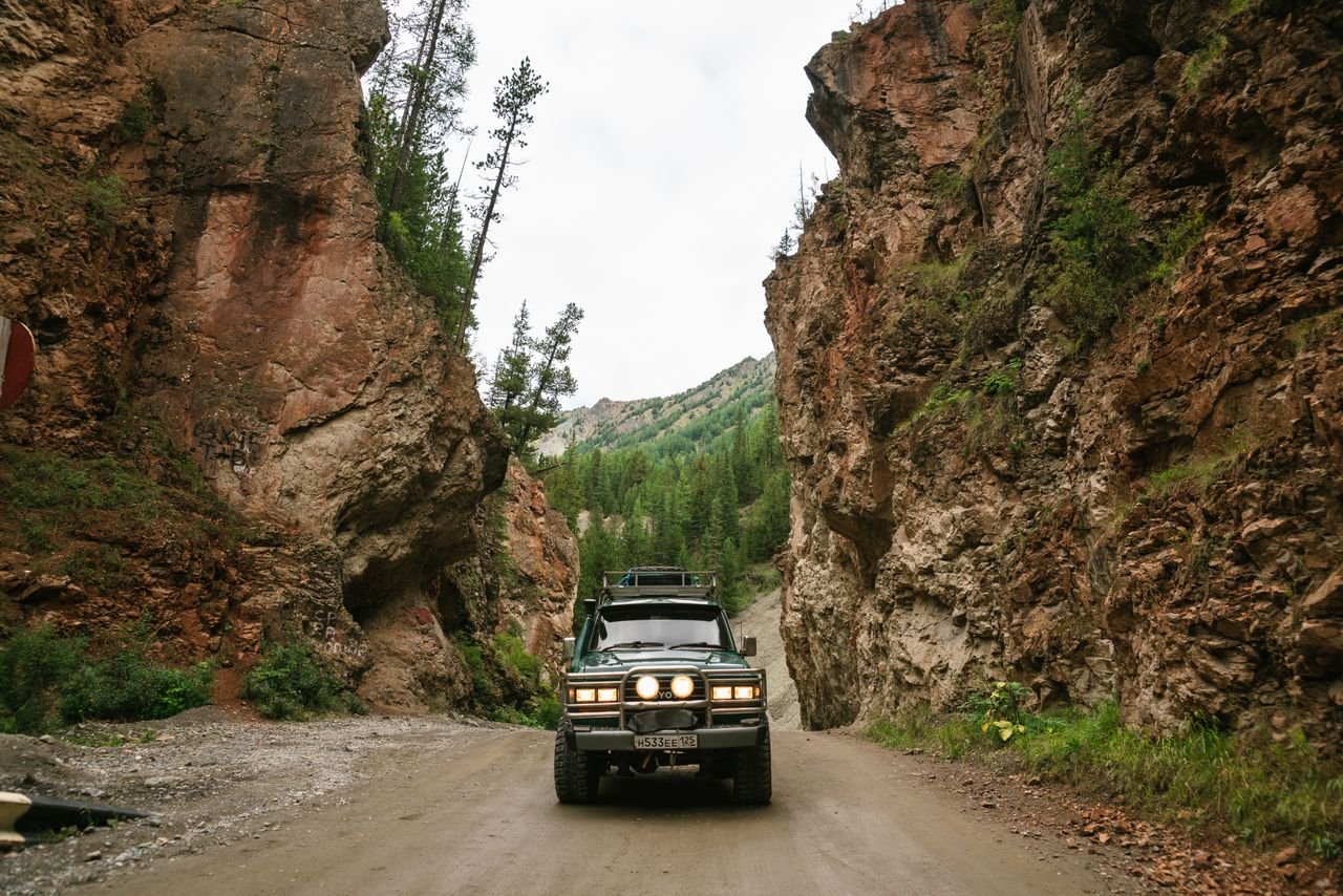 Off-road 4x4 driving through a narrow rocky canyon amid lush greenery.