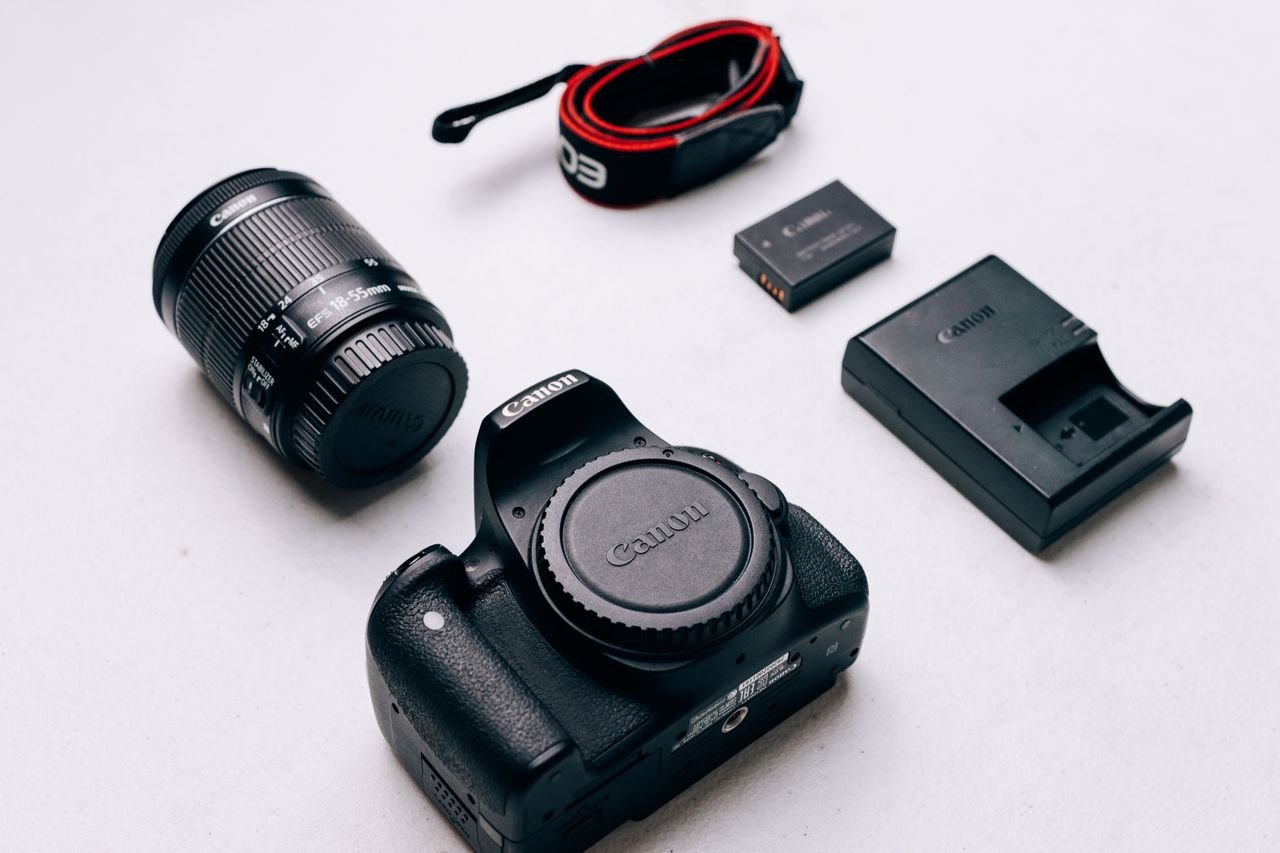 Flat lay of Canon DSLR camera accessories including lens, battery, and charger on a white background.