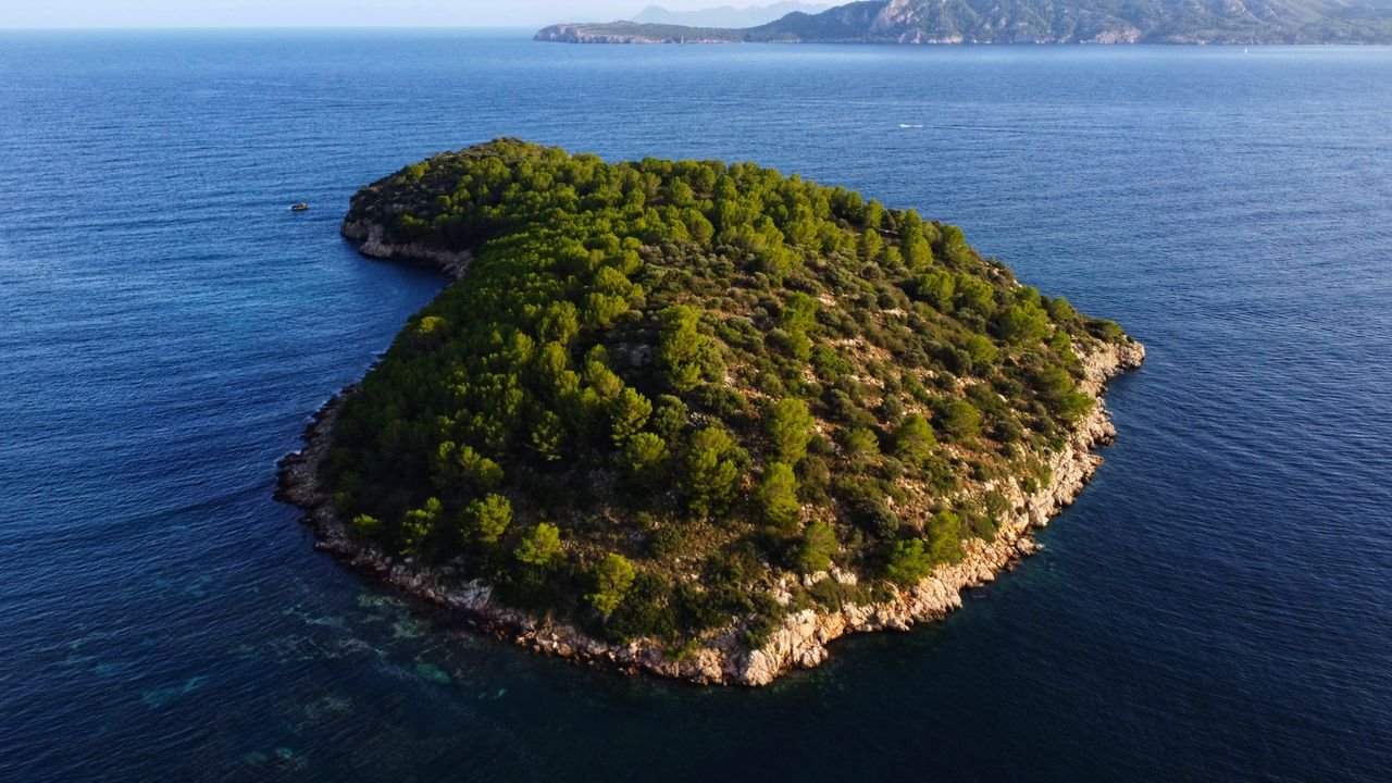 Stunning aerial shot of a lush green island surrounded by the blue Mediterranean sea.