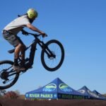 A mountain biker performs an impressive jump during a sunny day event at River Parks, showcasing skill and adventure.