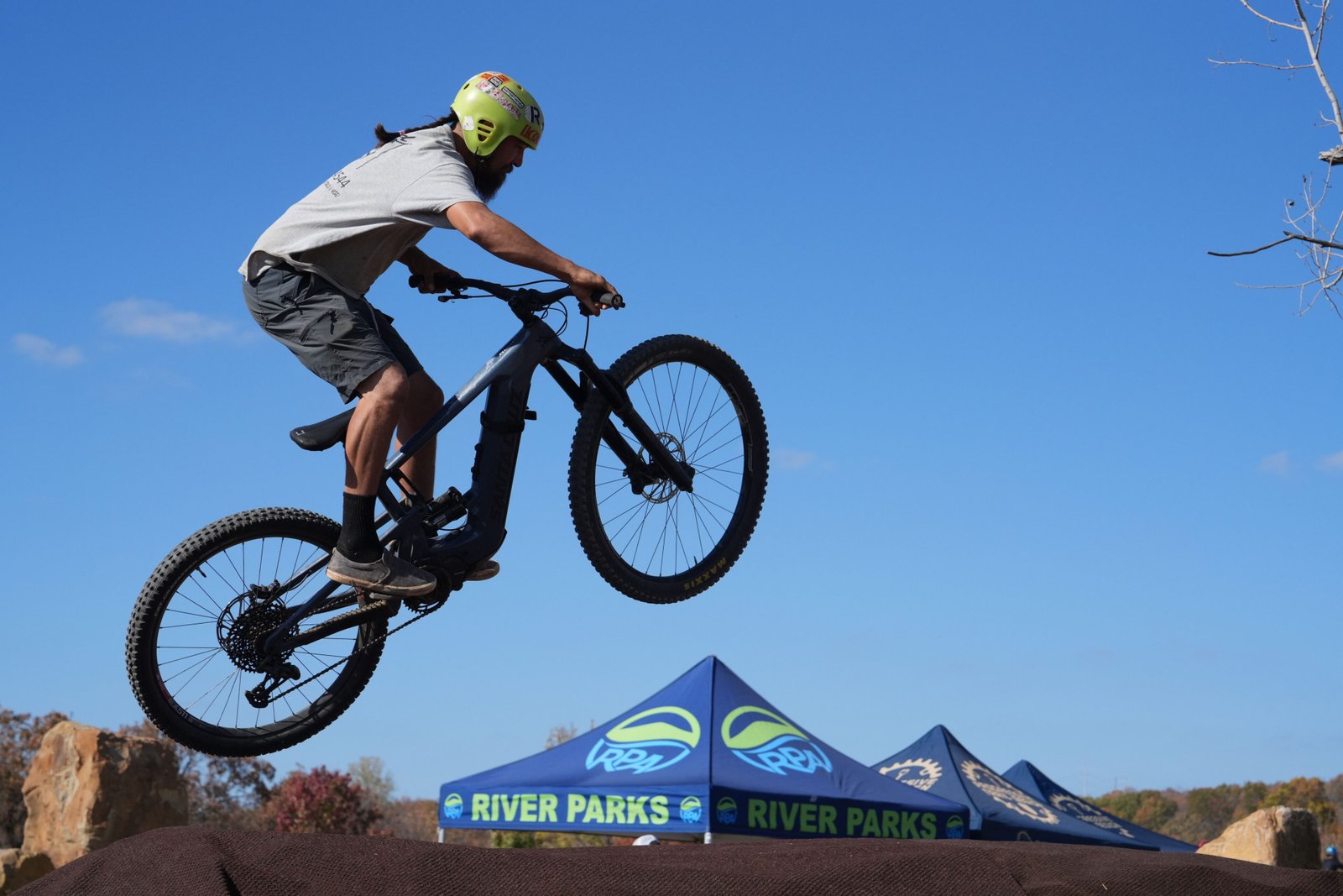A mountain biker performs an impressive jump during a sunny day event at River Parks, showcasing skill and adventure.